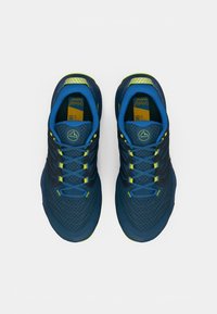 Μπλε αθλητικά παπούτσια με δικτυωτό άνω μέρος, υφή στο σχέδιο, κίτρινες λεπτομέρειες και αντίθετα κορδόνια. Μαξιλαρωμένη γλώσσα και λογότυπο στη φτέρνα.