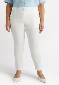 Pantalones blancos de stretch con cintura alta, cierre de dos botones y dobladillo a la altura del tobillo, combinados con tacones blancos puntiagudos. Textura suave.