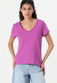 T-shirt kratkih rukava s V-izrezom u vibrantnoj ljubičastoj boji, izrađena od mekanog pamuka. U obliku kroja s lagano opuštenom siluetom i bez vidljivih uzoraka.