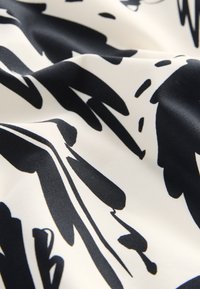 Glatka bijela tkanina s apstraktnim crnim uzorcima koje nalikuju potezima kistom i nježnim naborima.