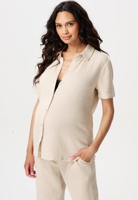 Hellbeige, strukturierte Kurzarm-Button-Up-Bluse mit entspannter Passform. Getragen über einem schwarzen Oberteil, kombiniert mit passenden Hosen mit Taschen.
