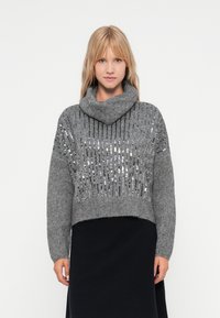Grå strikket genser med cowl-hals og kort design. Har vertikale rader av sølv paljetter foran og ribbet tekstur.