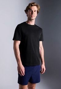 T-shirt preta de algodão com decote redondo, mangas curtas e corte descontraído, combinada com calções azul-marinho. Design simples, sem padrões.