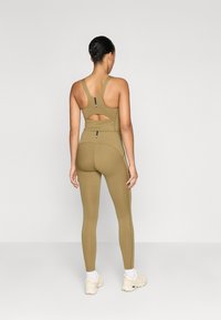 Olivno zelena športna oblačila, ki vključujejo oprijet zgornji del s športnim hrbtom in izrezom ter hlače z visokim pasom, izdelana iz raztegljivega materiala.