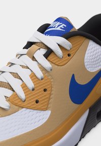 Μπεζ, λευκό και μπλε αθλητικό παπούτσι Nike με λευκά κορδόνια, μπλε σήμα Swoosh και υφασμάτων με υφή και συνθετικές επιστρώσεις.