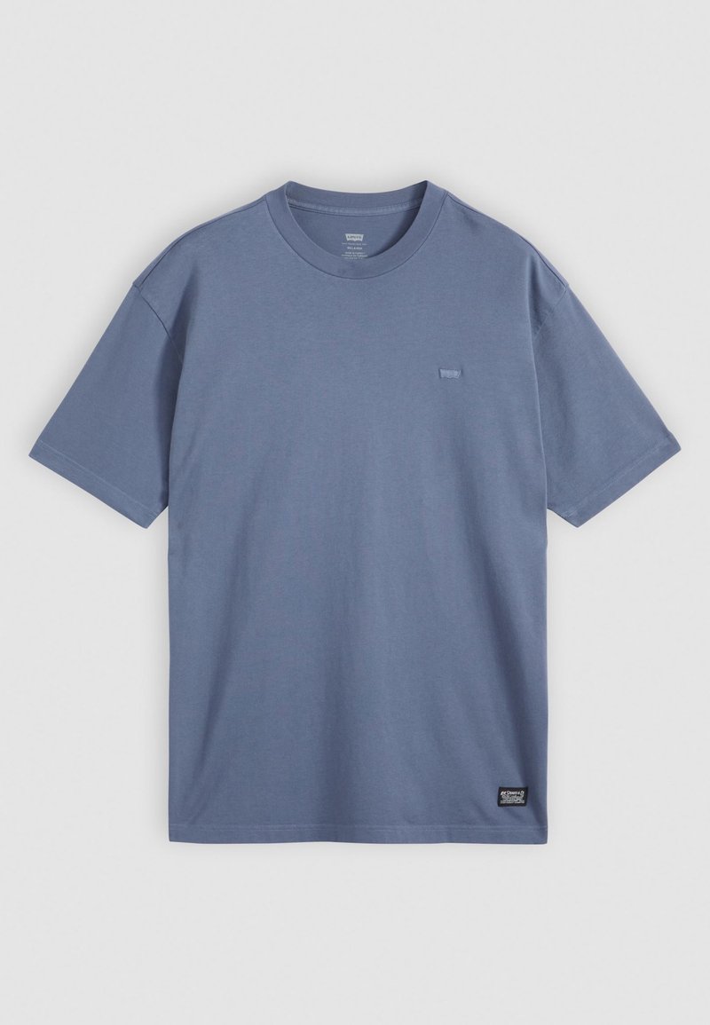Camiseta de algodón azul con mangas cortas y cuello redondo. Presenta un pequeño logo en el pecho y una etiqueta en la parte inferior izquierda.