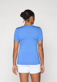 Camisa azul de manga curta feita de tecido suave, com decote redondo e um design ajustado, combinada com calções brancos.