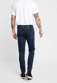 Mörkblå denimjeans med smal passform, utrustade med en läderlapp vid midjan, subtila sömdetaljer och kontrastsömmar.