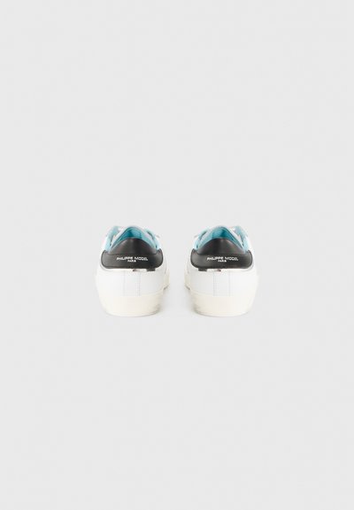 Baskets blanches avec un talon noir et des accents bleu clair ; matériau en cuir lisse, semelle plate et logo à l'arrière.