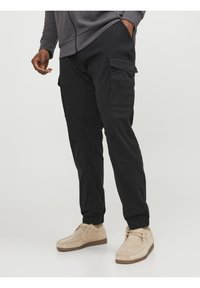 Zwarte cargobroek met elastische boorden en zijzakken, gemaakt van zachte stof. Gemaakt in combinatie met beige suede schoenen.