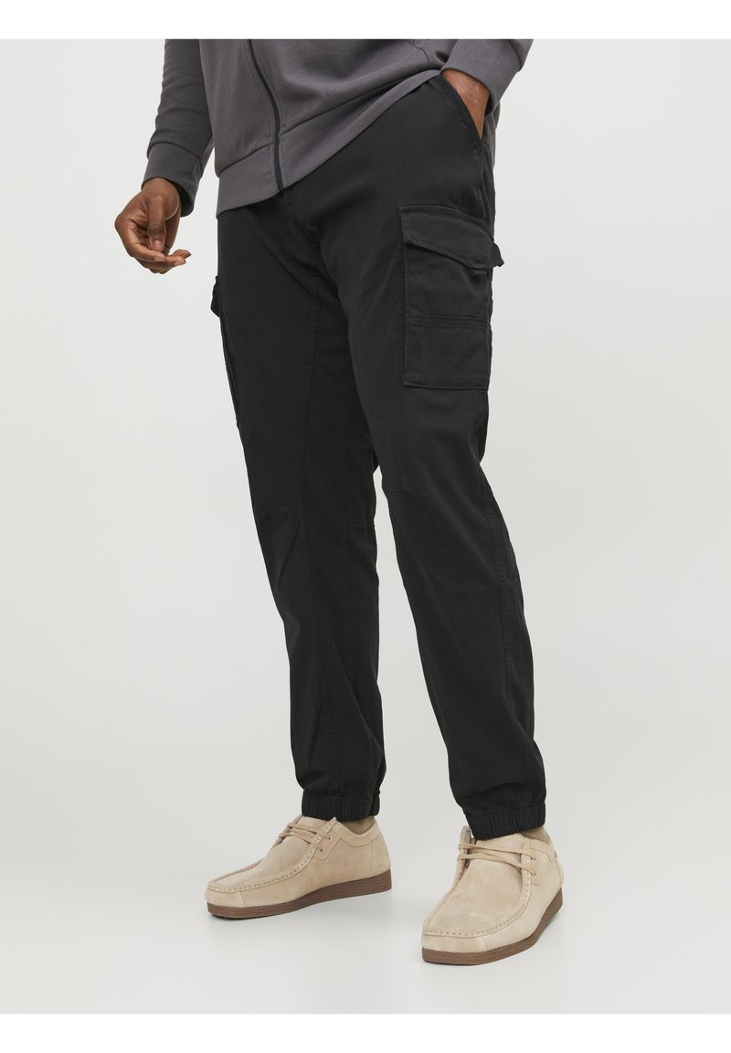 Zwarte cargobroek met elastische boorden en zijzakken, gemaakt van zachte stof. Gemaakt in combinatie met beige suede schoenen.