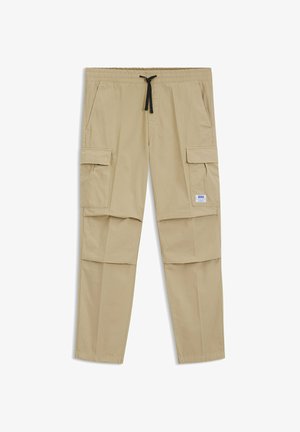 Pantaloni cargo beige con vita elastica e coulisse nera, caratterizzati da tasche con pattina laterali e una piccola etichetta bianca del marchio sulla tasca destra.