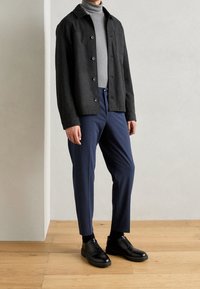 Czarna wełniana kurtka z guzikami, szary golf, granatowe spodnie oraz czarne sznurowane buty. Gładkie tekstury i uporządkowany fason.