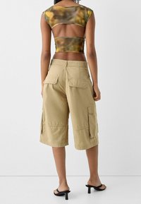 Klippt, flerfärgad topp med korta ärmar och öppen rygg, kombinerad med beiga cargoshorts med flera fickor och avslappnad passform.