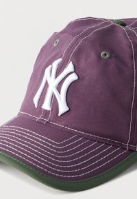 Μωβ καπέλο του μπέιζμπολ με πράσινο περιθώριο στο γείσο, λευκή ραφή και ανάγλυφο λευκό λογότυπο NY στην μπροστινή όψη.