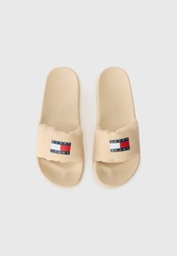Sandales à glissière beige avec une sangle rembourrée ornée d'un label logo rouge, blanc et bleu. Semelle en caoutchouc lisse et forme arrondie.