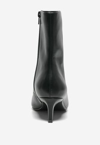 Botte en cuir noir à la cheville avec une fermeture éclair à l'arrière, bout pointu et talon fin, présentant une texture lisse et brillante.