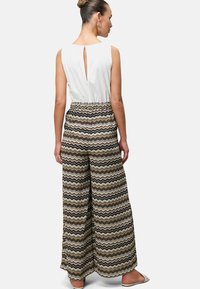 Un pantalon large présente un motif en zigzag de teintes terreuses, associé à un haut blanc avec une fente dans le dos. Tissu doux avec une taille élastique.