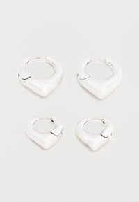 Kaks paari läikivaid hõbedasi rõngakujulisi kõrvarõngaid, millel on iseloomulik terav V-kujuline disain, esitatud valgel taustal.