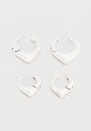 Dos pares de pendientes de aro plateados y brillantes con un diseño distintivo en forma de V puntiaguda, exhibidos sobre un fondo blanco.