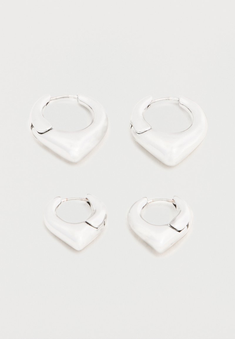 Deux paires de boucles d'oreilles créoles argentées brillantes avec un design distinctif en forme de V pointu, présentées sur un fond blanc.