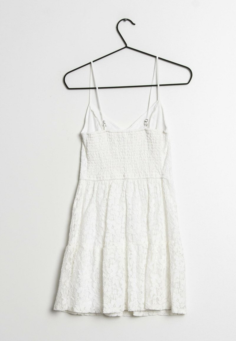 Weißes ärmelloses Kleid mit gerafftem Oberteil und gestuftem Spitzenrock, mit dünnen Trägern und einem Haken zum Aufhängen.