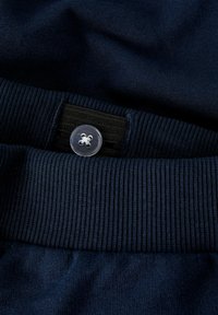 Mørkeblå ribbet linning med justerbar sort elastik og en klar firehuls knap til størrelsejustering.