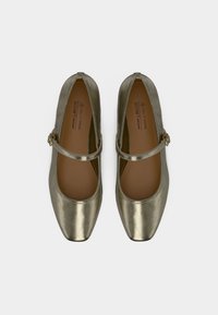 Μέταλλικά χρυσά παπούτσια Mary Jane με τετράγωνα μύτη και ρυθμιζόμενα λουράκια με αγκράφα, από φυτικό δέρμα, απεικονιζόμενα από πάνω.