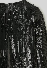 Robe noire ornée de sequins noir et argent créant un motif texturé et scintillant ; présente un dos en forme de cœur avec une fermeture à bouton.