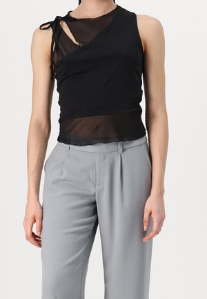 Sort ærmeløs mesh-top med asymmetrisk halsudskæring og bindedetalje, båret med højttaljede lysegrå plisserede bukser.