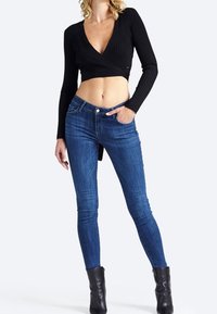 Top corto a maniche lunghe nero a coste abbinato a jeans skinny blu. L'outfit è completato da stivali neri alla caviglia.