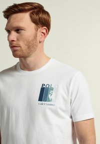 Camiseta blanca de algodón con un gráfico frontal que presenta el texto "POLO" y una ilustración de un jugador de polo en tonos de azul y verde. Mangas cortas.