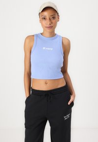 Kuttet lys blå ribbet tanktopp med hvit "Roxy" logo, parret med svarte joggebukser med brodert "New Balance" logo og snøring.