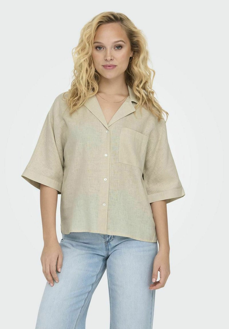 Beige linned skjorte med korte Ærmer, en afslappet pasform, krave, brystlomme og hvide knapper. Kombineret med lyseblå jeans.
