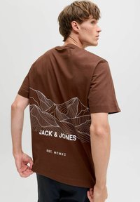 T-shirt en coton marron avec un graphique de contour de montagne blanc, le texte "JACK & JONES" et "EST. MCMXC" en dessous du design au dos.