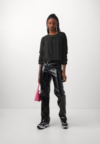 Black blouse with textured neckline, shiny black leather pants, pink handbag, and athletic sneakers with a white and black design.