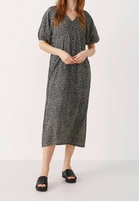Vestido de media longitud en negro con un estampado abstracto en blanco. Cuenta con mangas cortas abullonadas y un escote en V. Combinado con sandalias deslizantes negras.