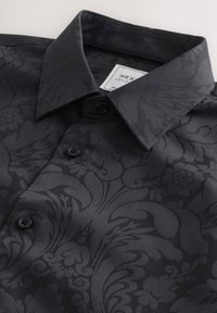 Camicia nera con motivo floreale, realizzata in tessuto liscio, con colletto appuntito e quattro bottoni coordinati sul davanti. Etichetta di cura visibile all'interno.