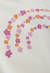 Vitt tyg med ett flerfärgat blommönster som innehåller rosa, lila och orange blommor, några prydda med guldaccenter, arrangerade i en regnbågsbåge.