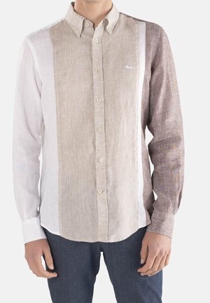 Mann trägt ein langärmeliges Hemd mit vertikalen Farbfeldern in Weiß, Beige und Braun, kombiniert mit dunkelblauer Hose.