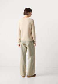 Beige textúrájú pulóver hosszú ujjal, világoszöld, bő szárú farmernadrággal és barna cipővel párosítva. Egyszerű, laza dizájn.