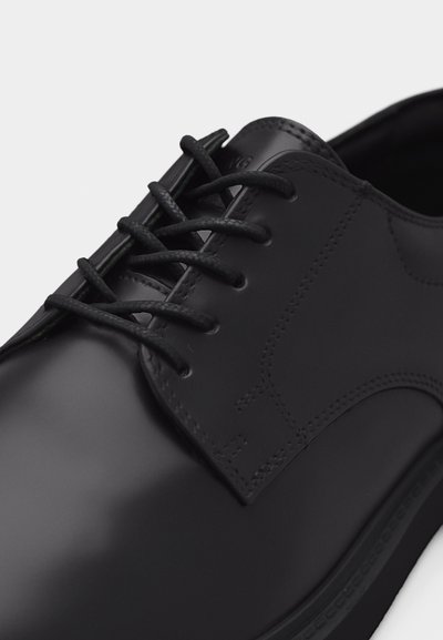 Μαύρο γυαλιστερό δερμάτινο παπούτσι για επίσημες εμφανίσεις με στρογγυλεμένη μύτη, κλειστό κορδόνι και λεπτομερή ραφή στο λείο επάνω μέρος και στην σόλα.