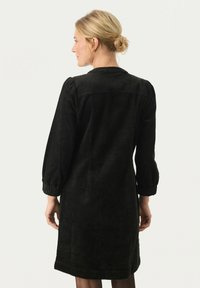Robe en velours côtelé noir à manches longues et à la silhouette légèrement ajustée. Présente un tissu texturé et des détails froncés au niveau des poignets.