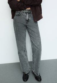 Vyötäröltä korkeat, löysät farkut mustavalkoisessa teksturoidussa kankaassa, joissa on kontrastivärisiä saumoja ja repsottavat helma yksityiskohdat. Yhdistetty mustiin kenkiin.