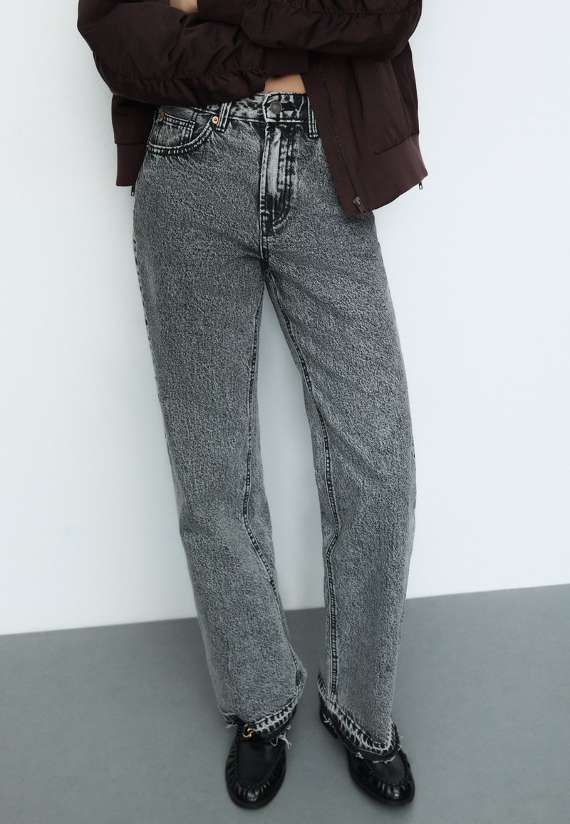 Vyötäröltä korkeat, löysät farkut mustavalkoisessa teksturoidussa kankaassa, joissa on kontrastivärisiä saumoja ja repsottavat helma yksityiskohdat. Yhdistetty mustiin kenkiin.