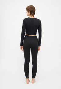 Svart tettsittende langermet topp og leggings laget av et glatt materiale. Toppen har et cropped design; leggingsene er hel lengde med høy midje.