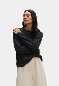 Ciemnoszara bluzka z długim rękawem i okrągłym dekoltem, wykonana z miękkiego materiału, zestawiona z jasnobeżowymi spodniami o luźnym kroju i kieszeniami.