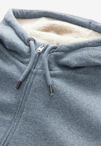Felpa con cappuccio azzurro chiaro, foderata in morbido pile bianco, dotata di zip e cordini con accenti metallici.