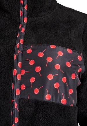 Čierna fleecová bunda s vreckom zo vzorovanej látky s červenými čerešňami. Zapínanie na zips vpredu, vysoký golier a mäkká štruktúra.
