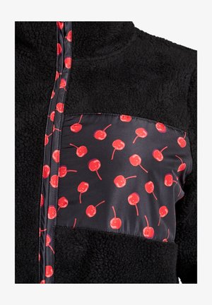 Veste polaire noire avec une poche en tissu à motif de cerises rouges. Fermeture éclair à l'avant, col montant, et texture douce.